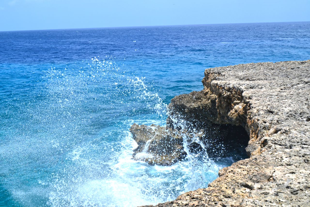 services-02 Vibrant ocean waves splashing against the rocky shoreline of Curaçao. A perfect tropical seascape for travel inspiration.